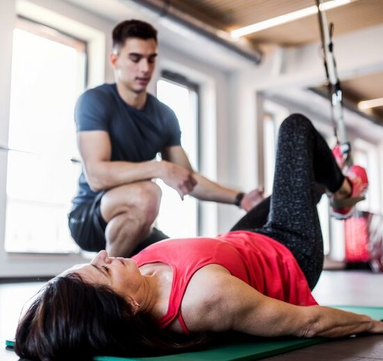 A senior woman in gym and a handsome personal trainer doing exercise with TRX.
